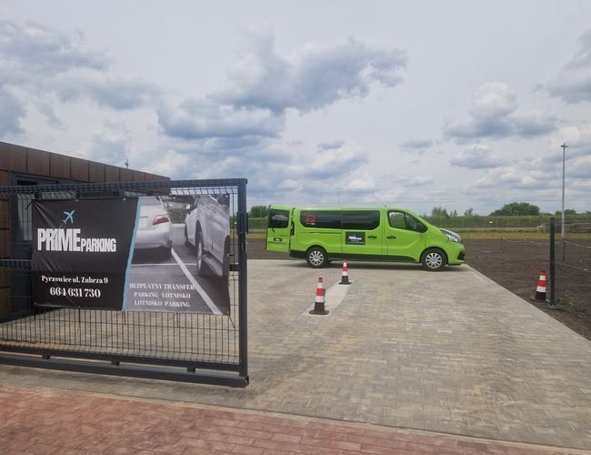 Parking Prime – Ogrodzony teren z bramą i reklamą. Na placu stoi zielony bus. Obok widoczny bruk i pachołki.