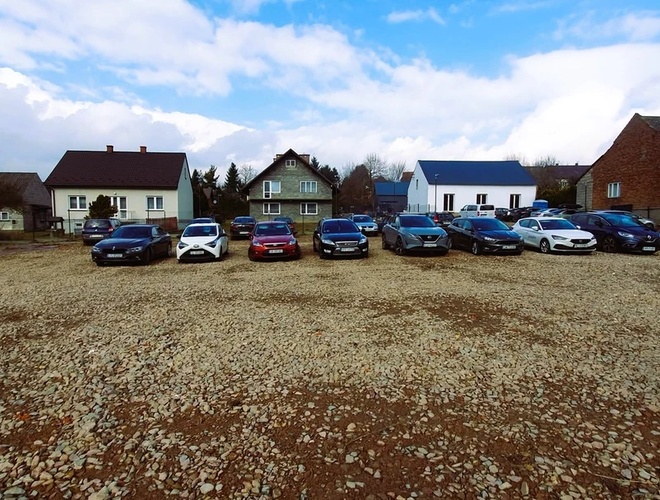 Parking Amber – Kamienisty plac z zaparkowanymi samochodami. W tle widoczne domy.