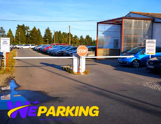 Wjazd na parking WE Parking z widocznym szlabanem i zaparkowanymi autami po obu stronach.