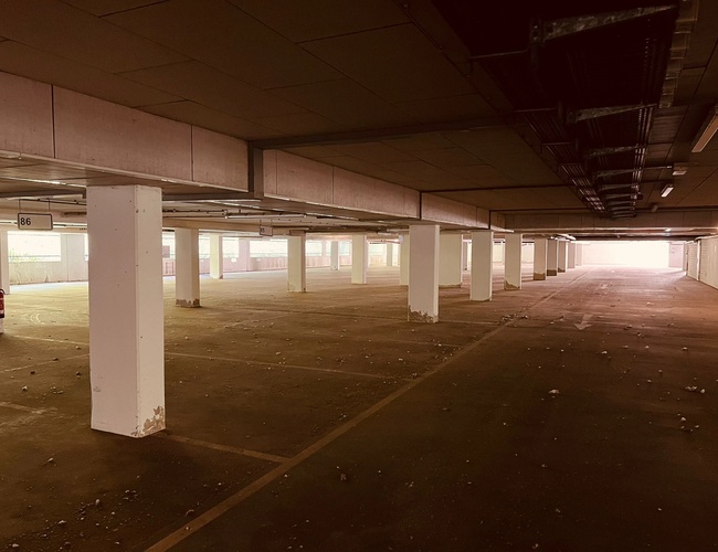 Sun Park Airport Parking Garage – Parking podziemny z betonowymi filarami. Pusta przestrzeń z widocznymi miejscami postojowymi. Światło wpada z daleka.