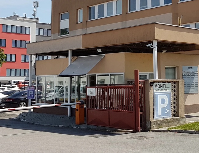 Budynek z wjazdem na parking, ogrodzony, z kilkoma samochodami zaparkowanymi przed wejściem.