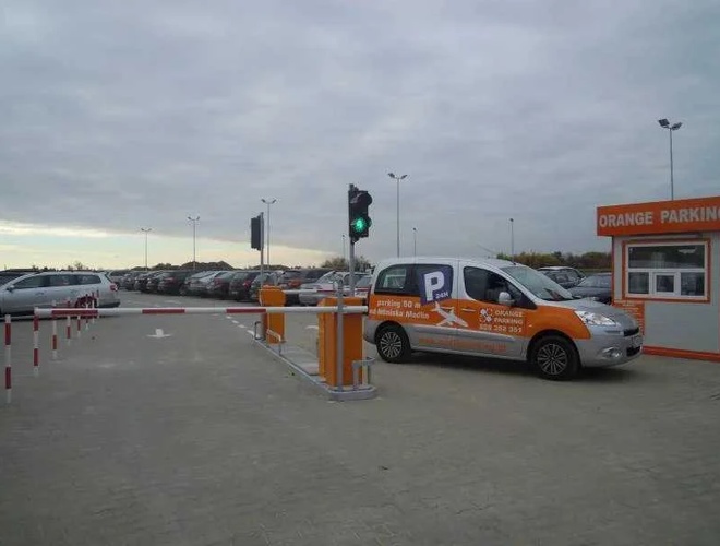 Orange Parking Modlin – El área está abierta y bien iluminada. El auto se detiene en la barrera de entrada. Al lado hay una caseta de aparcamiento.