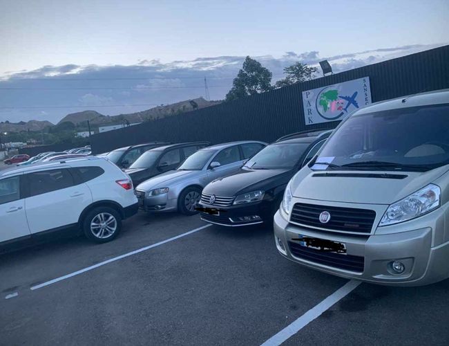 PARK SANSECAR VALET - El estacionamiento está lleno de autos. Al fondo se observa un cartel con el logo. El área está cercada y es espaciosa.