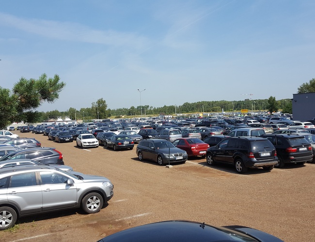 AAP-66 – Parking pełen samochodów na otwartej przestrzeni. Na granicy terenu rośnie kilka drzew.