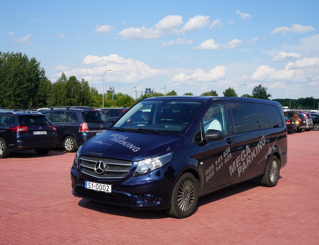 VIP Garáže MEGA Parkovisko – Na námestí stoja autá. Pozemok je spevnený a priestranný. V pozadí sú vidieť stromy.