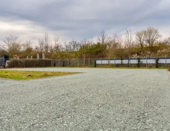 Valet de aparcamiento de autobús – el aparcamiento es cerrado y espacioso. En el sitio se puede ver una superficie de grava y algunos árboles.
