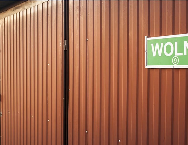 PERI Parking Garaże Premium – Czerwona brama garażu z tabliczką. Na tabliczce napis "Wolny". Jest również oznaczenie liczby.