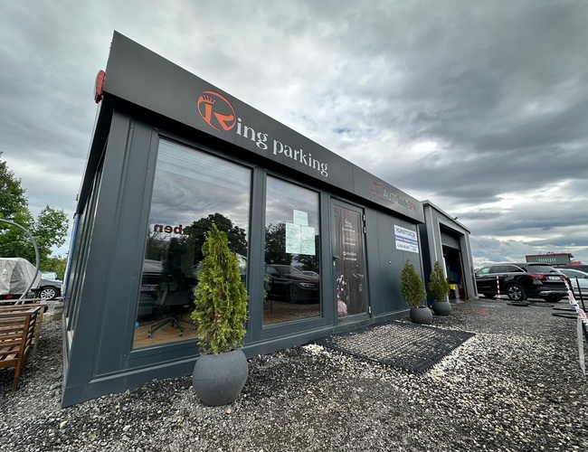 Kraków KING parkovanie – Viditeľná sivá búdka zákazníckeho servisu. Pred ňou rastú zelené rastliny v kvetináčoch.