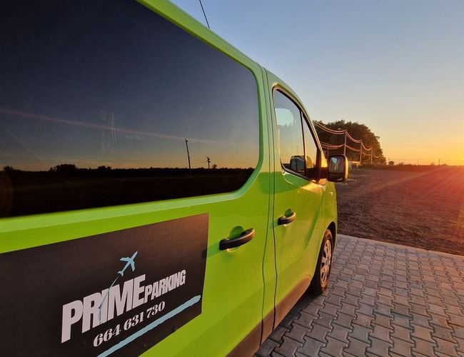 Parking Prime - Zielony van stoi na wyłożonym kostką placu. W tle widać zachód słońca.