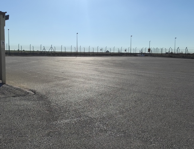 Parkovisko Odkryj-Auto - Veľké, oplotené nádvorie s lampami. Na ľavej strane zastrešené miesto. Na obzore viditeľný plot.