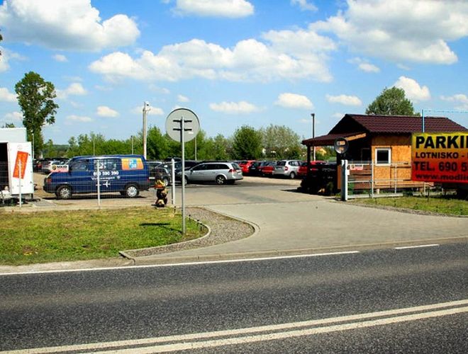 Parkoló P38 – A parkoló kerítéssel és világítással van ellátva. A besz opening vezet az információs fülkéhez. Néhány autó áll a téren.