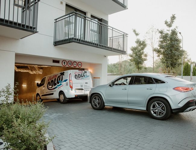 Abflug Garage – unterirdischer Parkplatz mit vielen Autos. Die Betonsäulen haben gelb-schwarze Warnbänder. Die Beleuchtung sorgt für gute Sicht.
