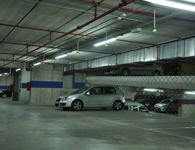 Oliveral Parking - Zamknięty parking podziemny. Oświetlone miejsce ma dwa poziomy. Na obu poziomach stoją samochody.