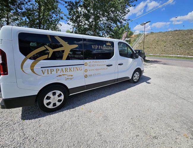 VIP-Parkplatz - an der S2-Strecke. Ein weißer Bus mit Firmenlogo steht auf dem Kiesplatz. Im Hintergrund sind Bäume und Beleuchtung.