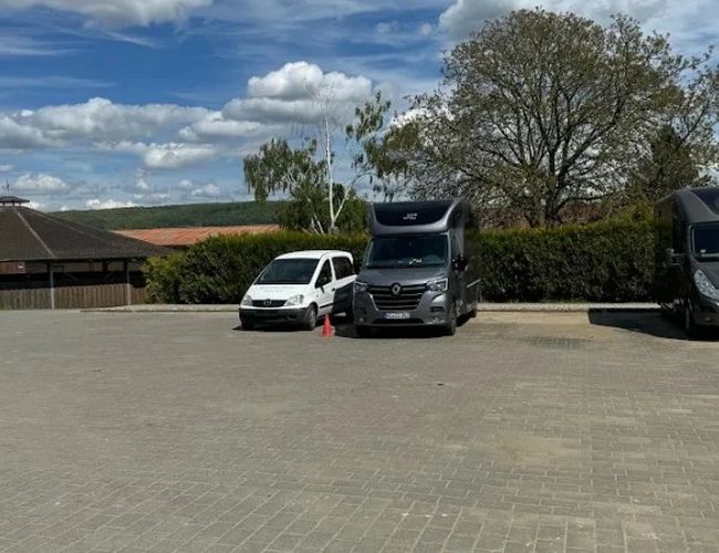 Parking ParkNow Frankfurt - Plac jest pusty i przestronny. Widoczne są dwa zaparkowane samochody. W tle rosną drzewa.