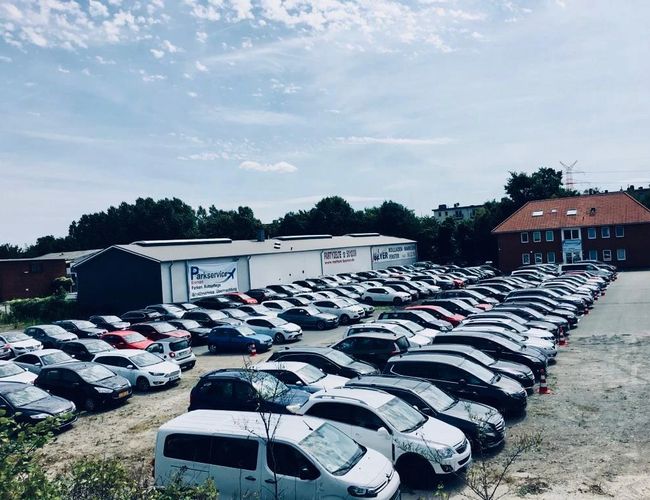 Aparcamiento Parkservice Bremen Valet. Coches alineados en una zona pavimentada, en el fondo un edificio administrativo.