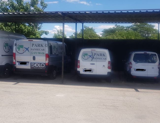 PARK SANSECAR VALET – En el aparcamiento techado hay tres vehículos de entrega blancos. Cada uno de ellos tiene el logo de la empresa en las puertas. Los vehículos están alineados uno al lado del otro.