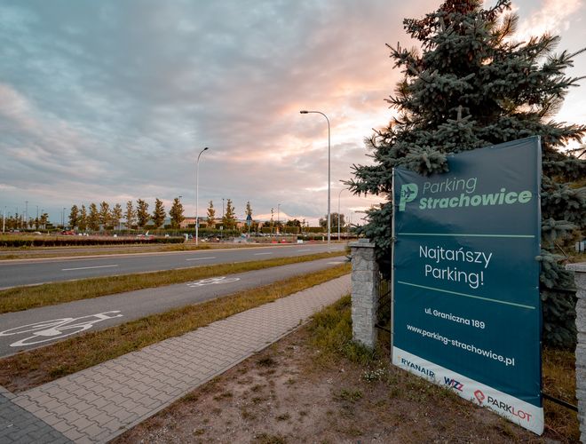 Parking Strachowice – widoczny jest baner reklamowy obok ścieżki rowerowej. W tle widnieje jezdnia i roślinność.