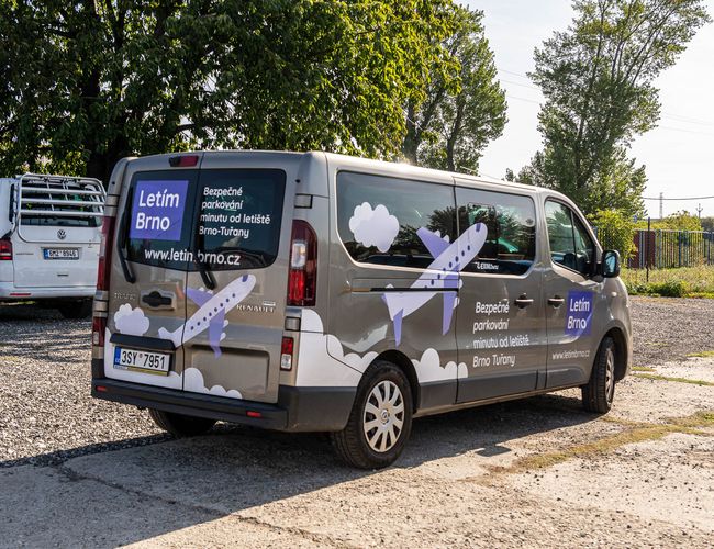 Parking Letim Brno – Na parkingu stoją dwa samochody. Minibus z logo parkingu. W tle widać drzewa i ogrodzenie.