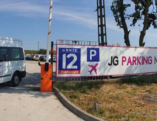 JG Parking – Furgon blanco junto a la entrada con barrera. Al lado se puede ver un gran cartel informativo.