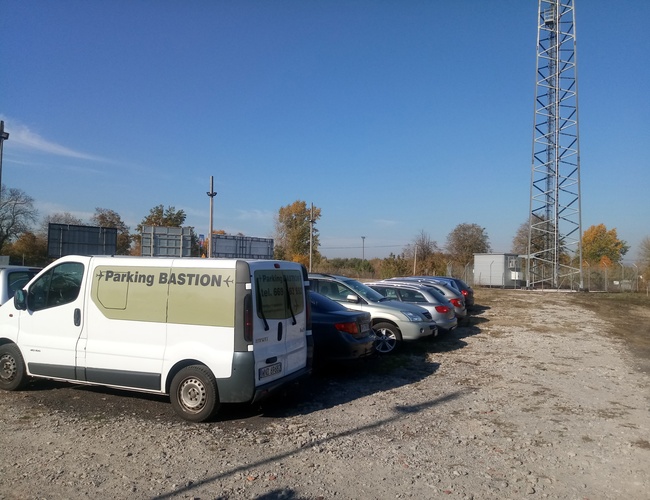Parking Bastion - El área está cercada y abierta. Los coches están en fila. Al lado hay una furgoneta blanca.