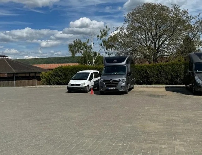 Parkovanie ParkNow Frankfurt - Námestie je prázdne a priestranné. Sú viditeľné dve zaparkované autá. Na pozadí rastú stromy.