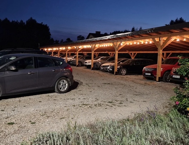 Parkovisko PARK4YOU - Večerná fotografia krytého parkoviska. Vozidlá stoja pod dreveným prístreškom. Jemné osvetlenie vytvára príjemnú atmosféru.