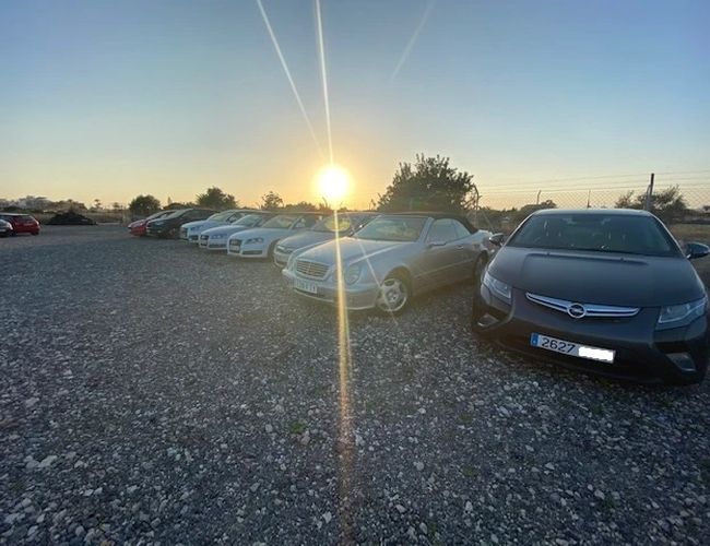 The Best Parking Alicante Outdoor Valet – Samochody stoją w rzędzie na żwirowym placu. Po lewej widać zachodzące słońce.