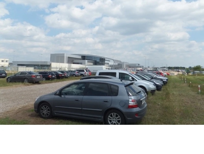 VALET Parking – fila de coches aparcados en una superficie de césped. Al fondo, un gran edificio. El área no está cercada.