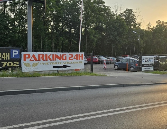 Victory Cars - Parking 24h se encuentra en una carretera concurrida. Está cercado y bien iluminado. Al lado, hay varios coches aparcados.