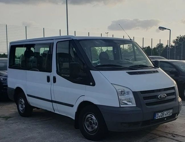 Parking Weltparking – Biały van stoi na parkingu. Obok niego znajdują się inne samochody. Wokół widać oświetlony teren.