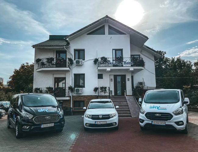 Parking Sky Park przy lotnisku w Iași – widok na teren parkingu przed budynkiem oraz samochody osobowe i bus transferowy Sky Park zaparkowane na posesji.