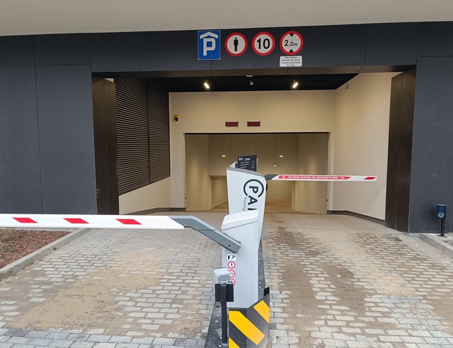 Atrium Garage – Vjazd s závorou a značkami. Cihlový koberec vedie dovnútra.