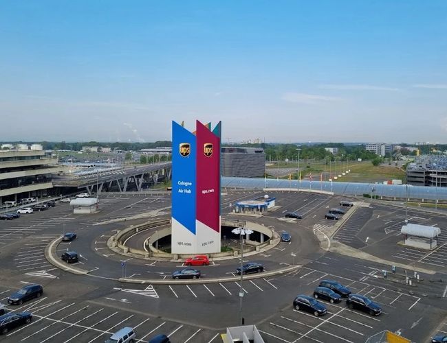 Panorama oficjalnego parkingu P1 na lotnisku Cologne Bonn z charakterystycznym pylonem informacyjnym oraz rozbudowanym układem dróg prowadzących do terminali.