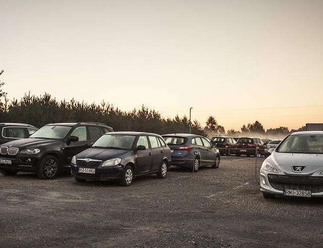 PERI Parking – En el aparcamiento de grava hay muchos coches. Todavía es una mañana temprana. Los árboles al fondo crean un límite natural.