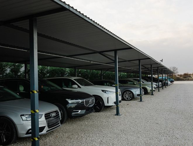 Zadaszony parking długoterminowy z rzędami samochodów osobowych zaparkowanych pod metalową wiatą