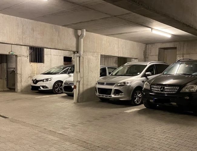 Parking Park2Travel Valet Garage - Parking podziemny, z oświetleniem. Trzy samochody stoją obok siebie. Betonowe ściany i podłoga.