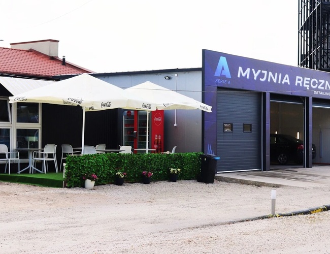 Najlepšia parkovacia séria A - Vedľa myčky sú stoly s slnečníkmi. Areál je štrkový. Na ľavej strane sa nachádza budova s pohovkami.