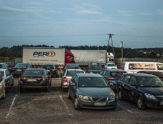 PERI Parking - Kilka samochodów stoi zaparkowanych obok siebie. Na końcu placu znajduje się ciężarówka. Parking jest ogrodzony.