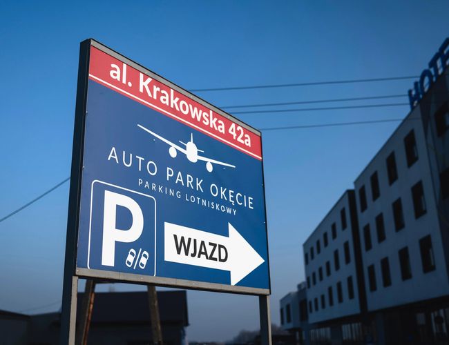 Auto Park Okęcie - duży znak drogowy z napisem „Wjazd”. Widoczny adres: al. Krakowska 42a. W tle budynki i hotel.
