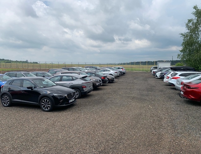 Estacionamiento con vista - En el estacionamiento hay coches aparcados. El área no está cercada. En el fondo se puede ver un amplio espacio.