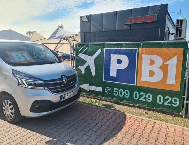 B1 Parking zadaszony - Pojazd stoi obok ogrodzenia. Na banerze widnieje duże logo parkingu.