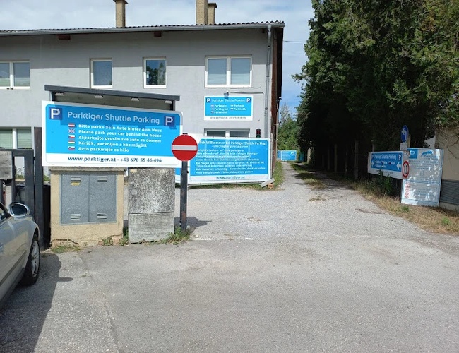 Transfer de Parking Parktiger – En la plaza de grava hay señales informativas. Al lado hay un edificio de color claro. El terreno está rodeado de árboles.