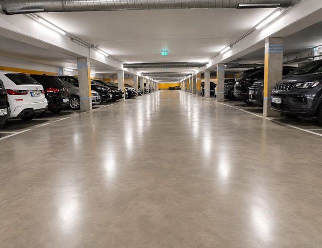 Zakręt wjazdowy na podziemny parking, betonowe ściany i jasne oświetlenie.