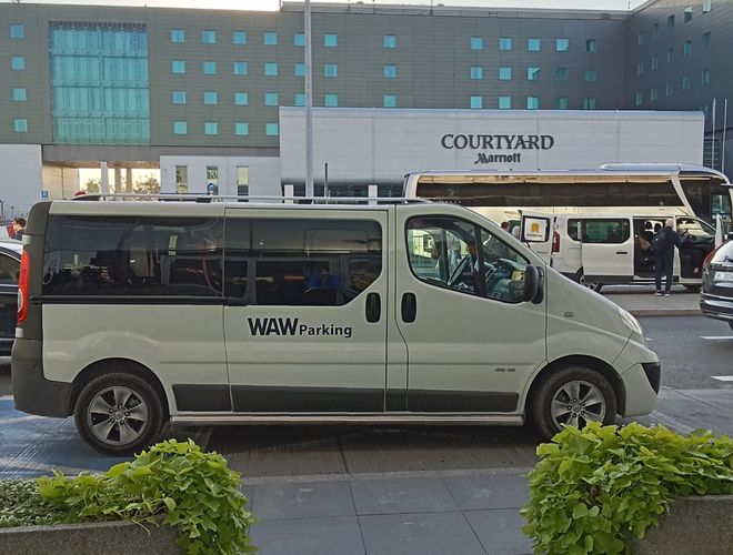 WAW Parking – Na zdjęciu bus przed hotelem. Budynek ma wiele okien. Obok znajduje się inny bus.