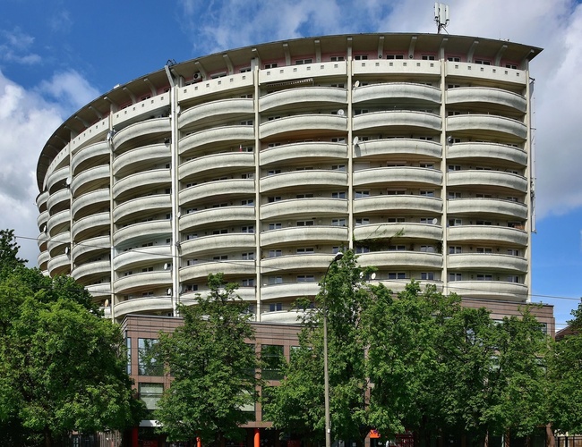 Parkering Colosseum - Det er en høy, rund boligbygning som er synlig. Før bygningen er det trær som vokser. Bygningen har mange balkonger.