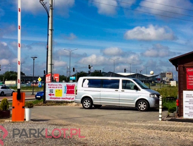 Parking Mega Park Service - Przez wjazd przejeżdża srebrny van. Obok są bramka i budka. Po prawej widoczny jest znak informacyjny.