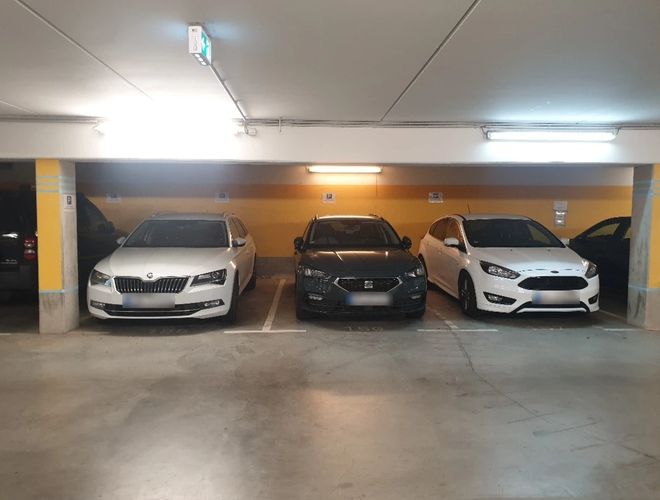 Trzy zaparkowane samochody na podziemnym parkingu, żółta ściana i sufit z oświetleniem LED.