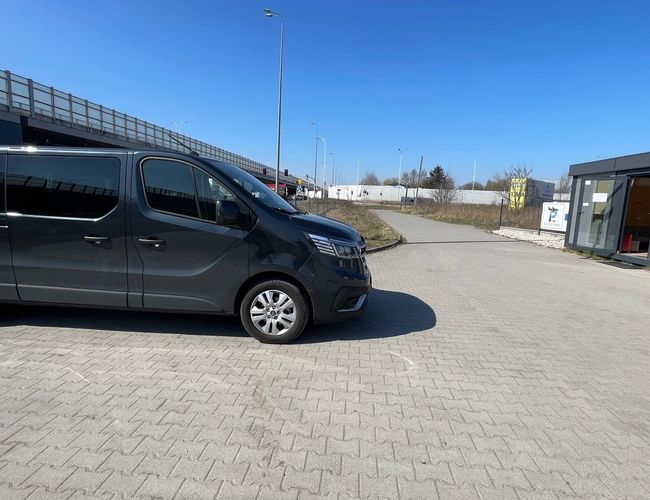 Parking Simple Park – obok biura stoi czarny van. Pokrywa niebieskie niebo. Teren jest otwarty i utwardzony.