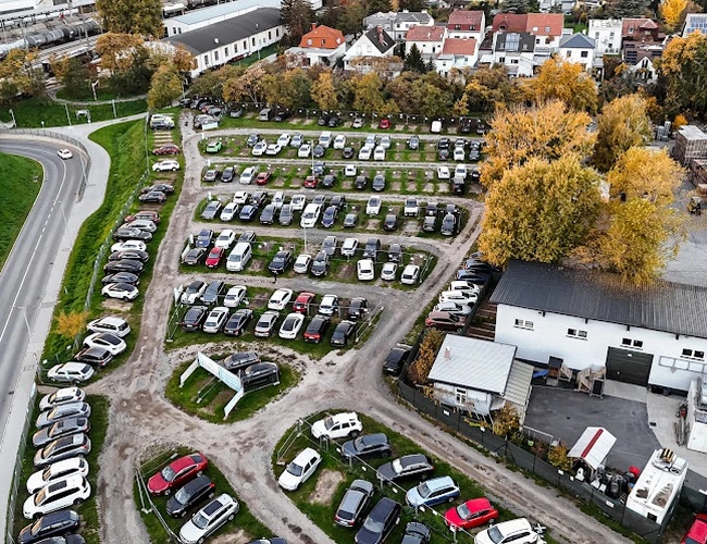 Estacionamiento de Aeropuerto Parktiger 1 - El área está llena de coches. El estacionamiento tiene espacios claramente señalizados. Está rodeado de árboles y edificaciones.
